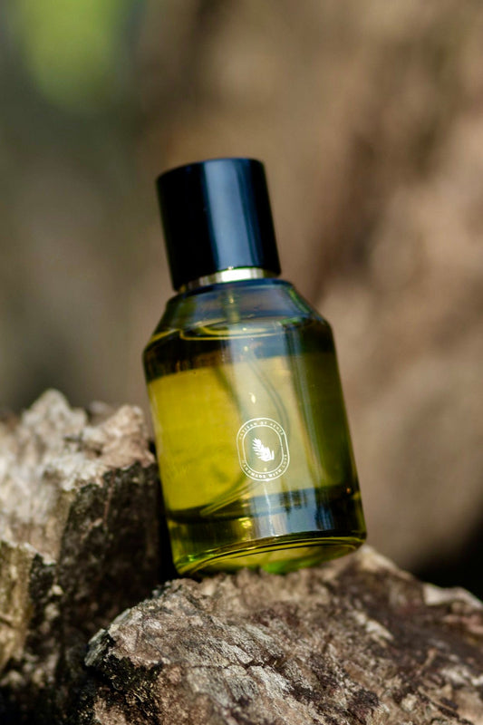 Olive green glass bottle of Artisan of Sense natural botanical room and body mist resting on rugged tree bark in a soft-focus forest setting.